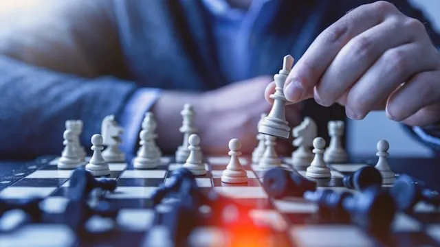A hand lifting a white chess piece on a board, a picture of planning one move at a time.
